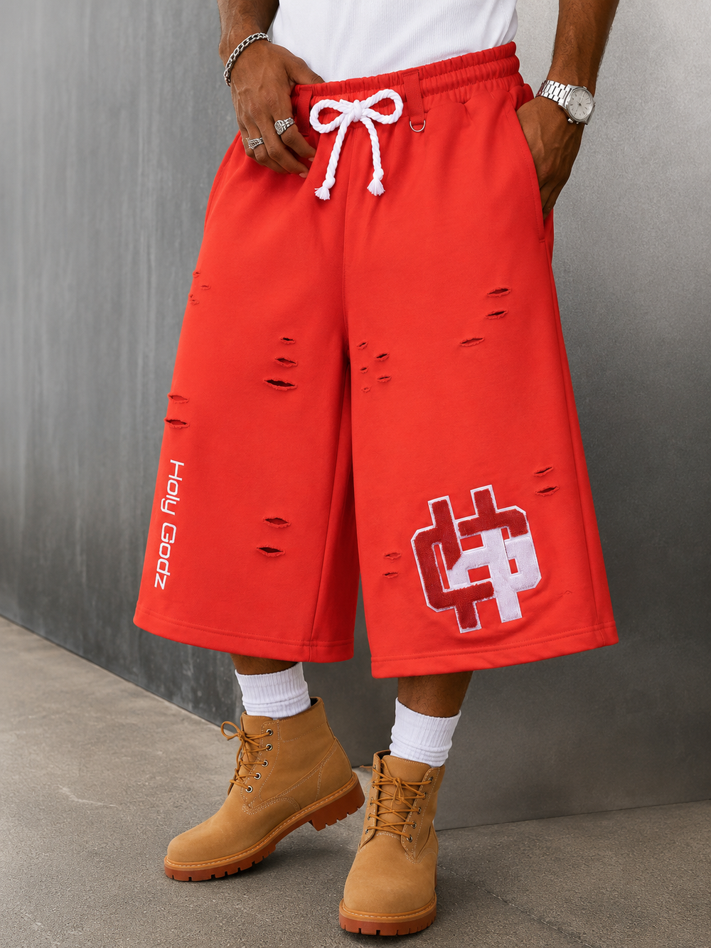 Holy Godz Built Diffrent Shorts in Acid Orange worn with boots — boxy 3/4 fit, distressed French terry, chenille HG patch
