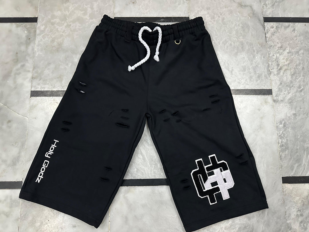 Holy Godz Built Diffrent Shorts in Washed Black — flat lay showing distressed slashing, chenille HG patch on the right leg and embroidered Holy Godz wordmark on the left